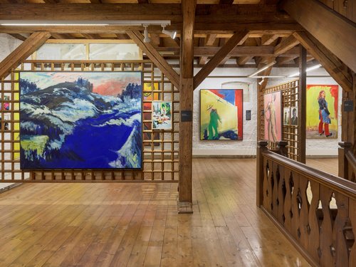 Blick in ein Kunstmuseum mit großflächigen bunten Bildern, Holzboden und greigelegtem Gebälk